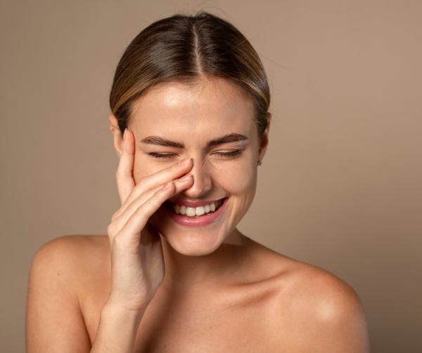 Woman laughing with her eyes closed and her hand resting on her cheek against a beige background