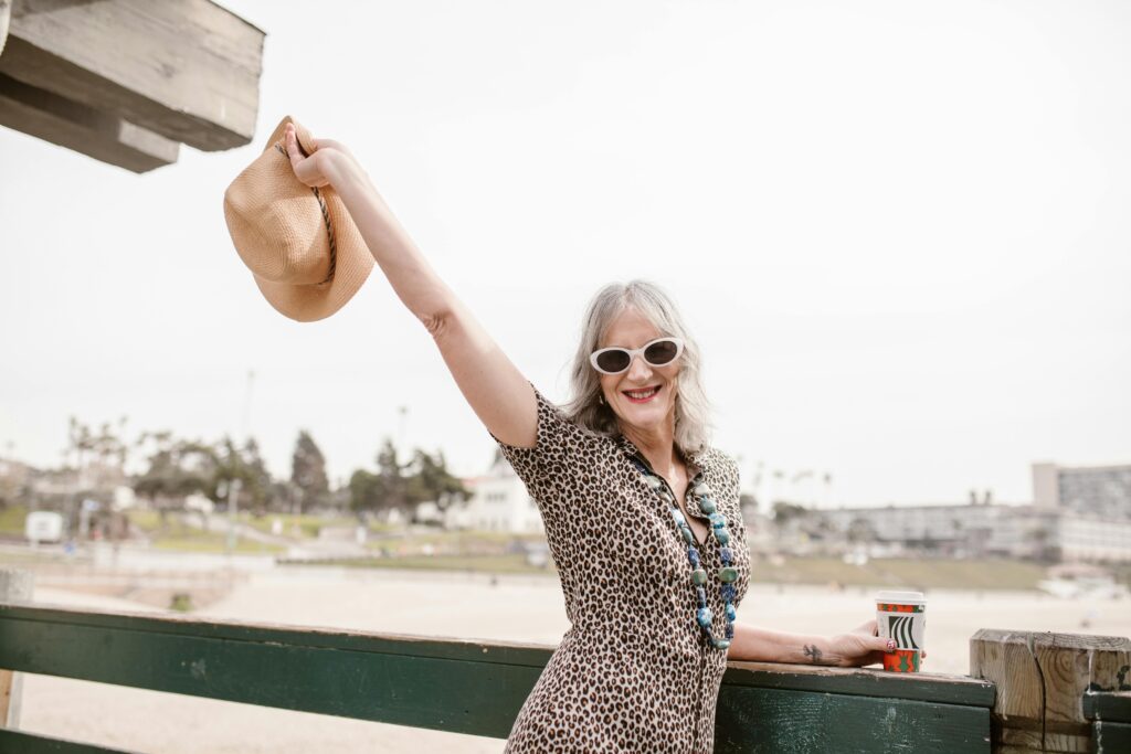 Woman standing next to railing holding a coffee and holding her hat in the air