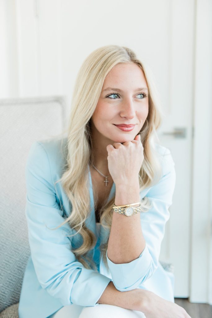 Doty Malouf, medical aesthetician at Women's Wellness of Mississippi, seated in a light grey armchair resting her chin on her hand