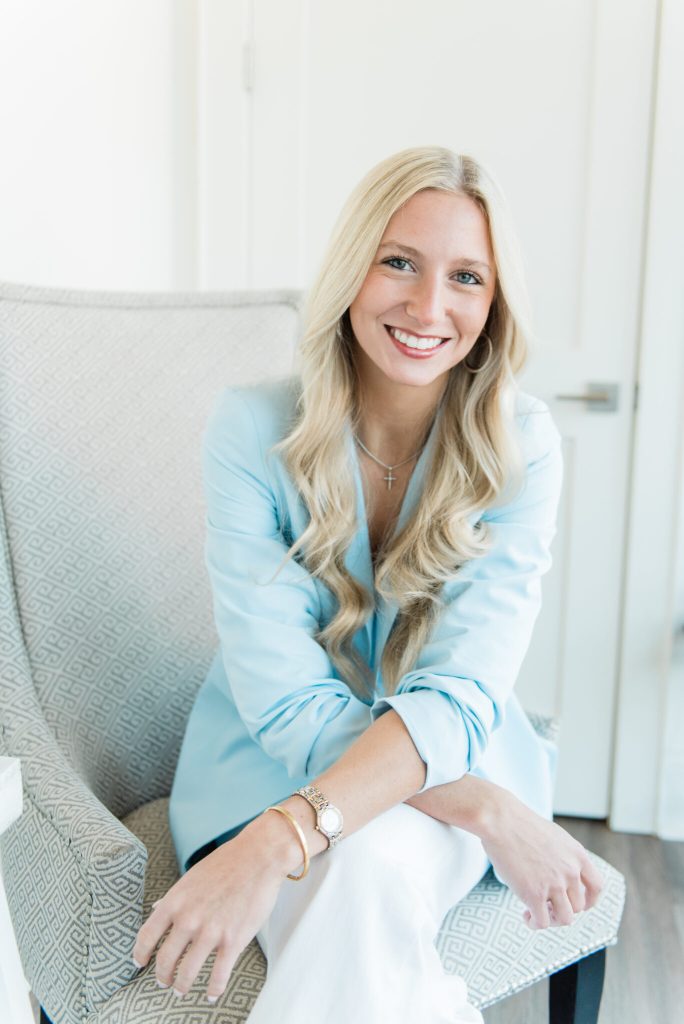 Doty Malouf, medical aesthetician at Women's Wellness of Mississippi, smiling while seated in a patterned armchair
