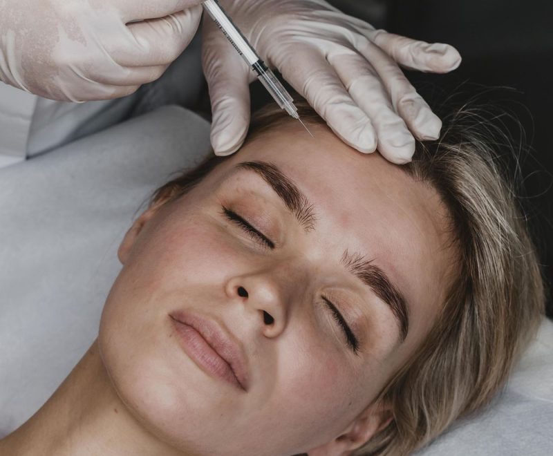 Practitioner in gloves giving a cosmetic injection to a woman's forehead